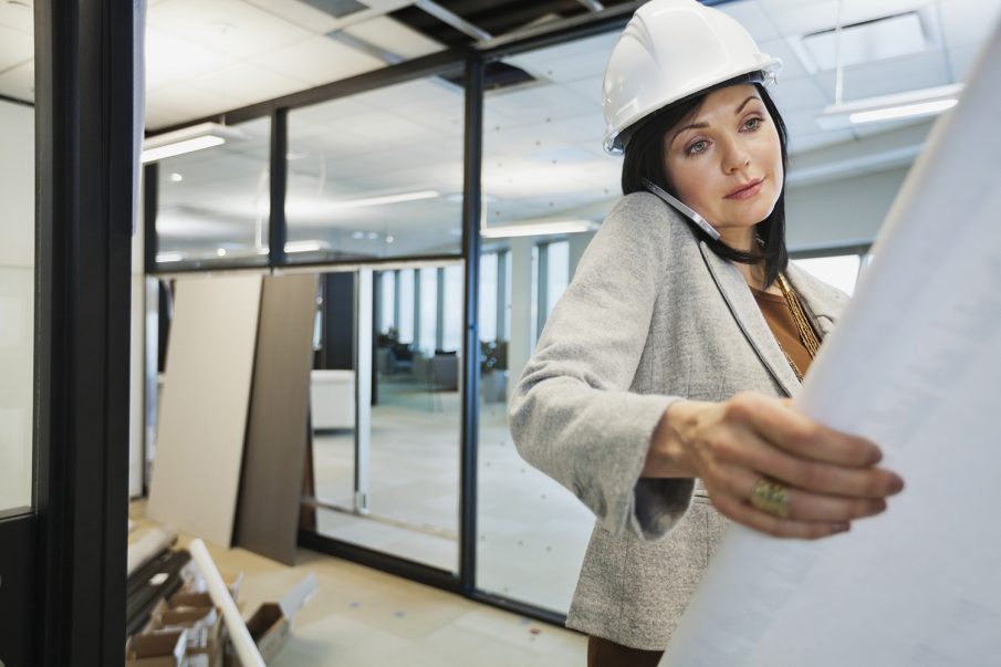 Female architect looking at blueprints while on smartphone.